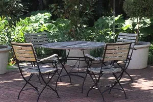 Outdoor patio set with a round table and four wooden chairs surrounded by plants