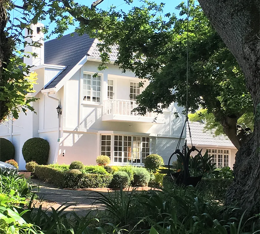 White house with a garden trees and a swing in the foreground