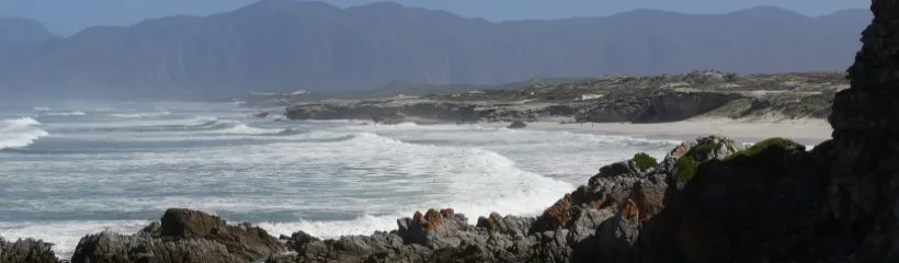 Rocky coastline with waves crashing against rocks and distant mountains