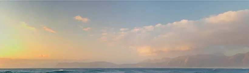 Sunset over the ocean with distant mountains and scattered clouds in the sky