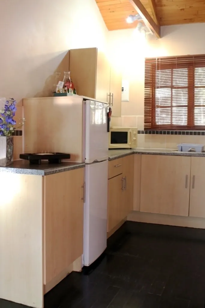 Kitchen with wooden cabinets white fridge microwave and window with wooden blinds