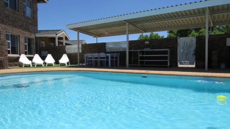 Swimming pool with lounge chairs covered patio and brick buildings in the background