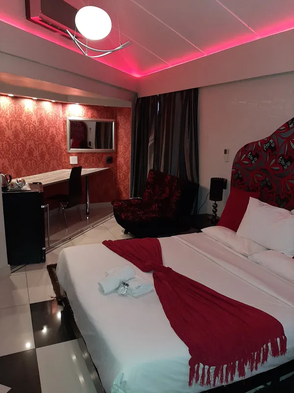 Modern hotel room with red and black decor bed desk and armchair