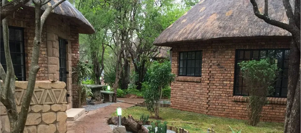 Pathway between two brick and thatch buildings with greenery in a natural setting