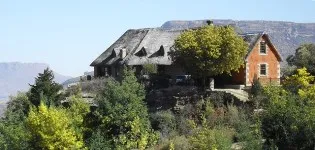 Rustic house with a thatched roof surrounded by trees and mountains
