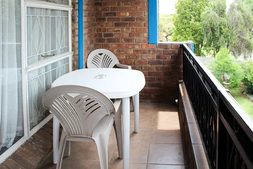 White plastic table and chairs on a brick balcony with a garden view