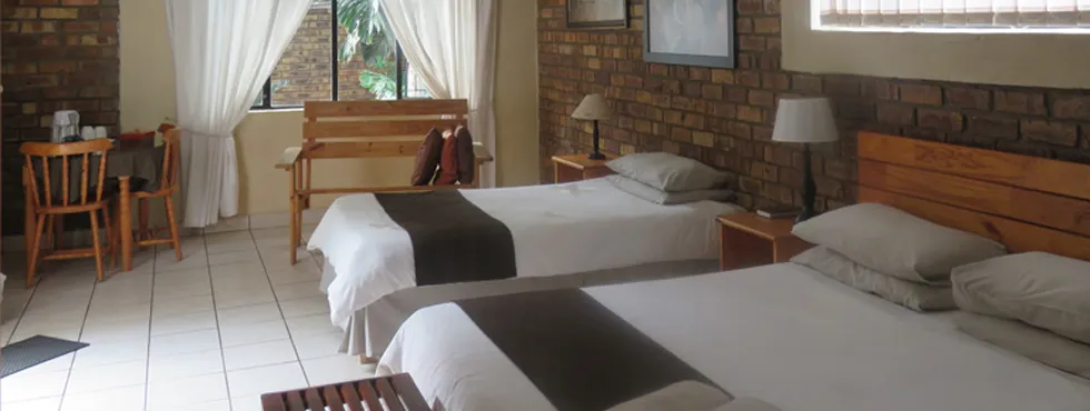 Two beds in a brickwalled room with wooden furniture and a window