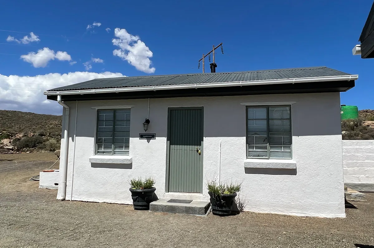 Small white house with green door two windows and potted plants outside