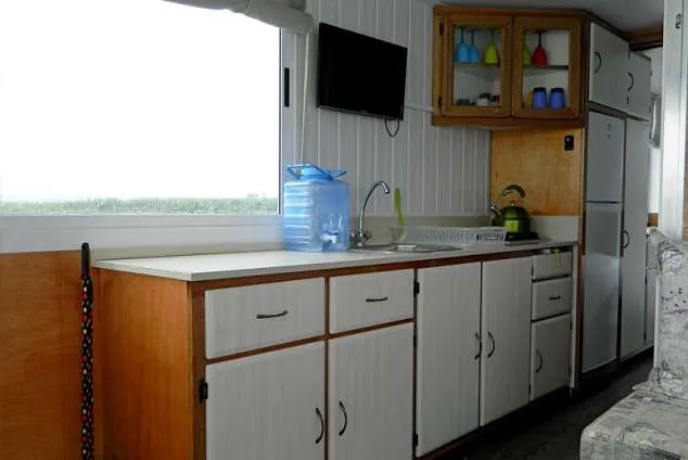 Compact kitchen with white cabinets sink and large window on a boat