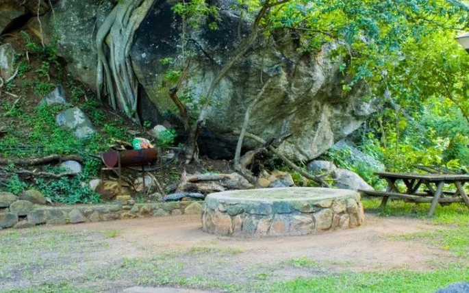 Stone well and picnic table in a forested area with rocky outcrops