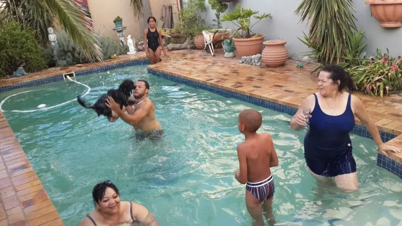 People and a dog playing in a swimming pool in a backyard