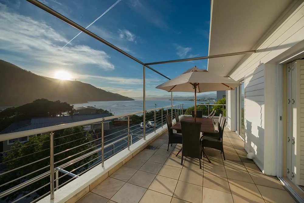 Balcony with table chairs and umbrella overlooking a scenic sunset and mountains