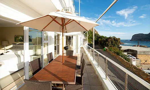 Wooden table with chairs on a balcony overlooking the ocean under a large umbrella