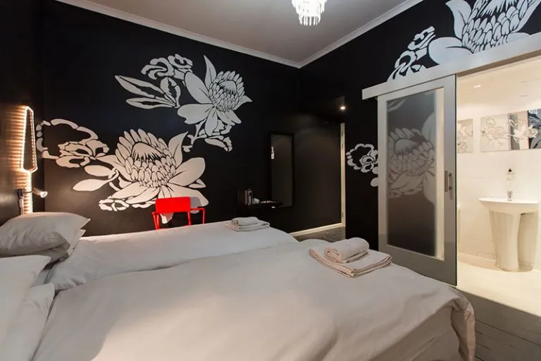 Two beds in a modern room with floral wall art and an open bathroom
