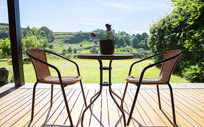 Two chairs and a small table on a wooden deck overlooking a green field