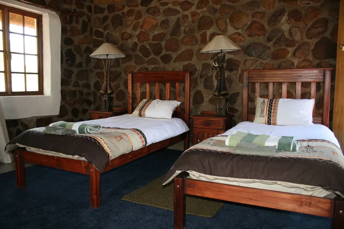 Two wooden beds in a rustic stonewalled room with blue carpet