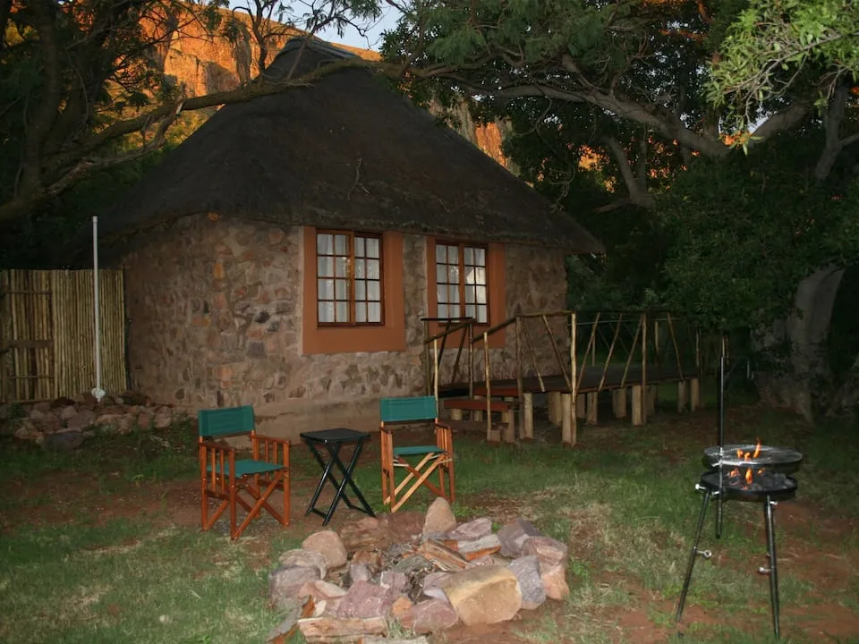 Stone hut with chairs fire pit and barbecue grill in a wooded area