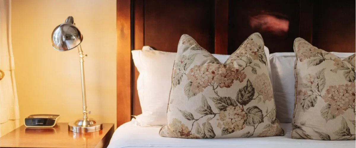 Two floral pillows on a bed with a bedside lamp on a nightstand