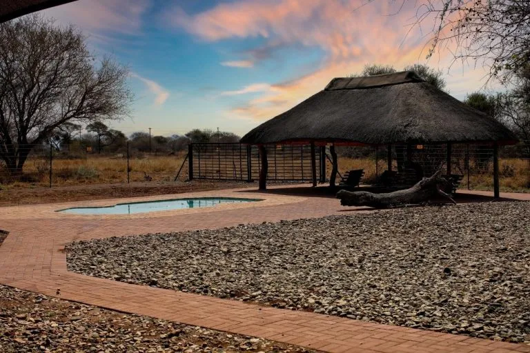 Thatchedroof hut with pool in a natural setting at sunset