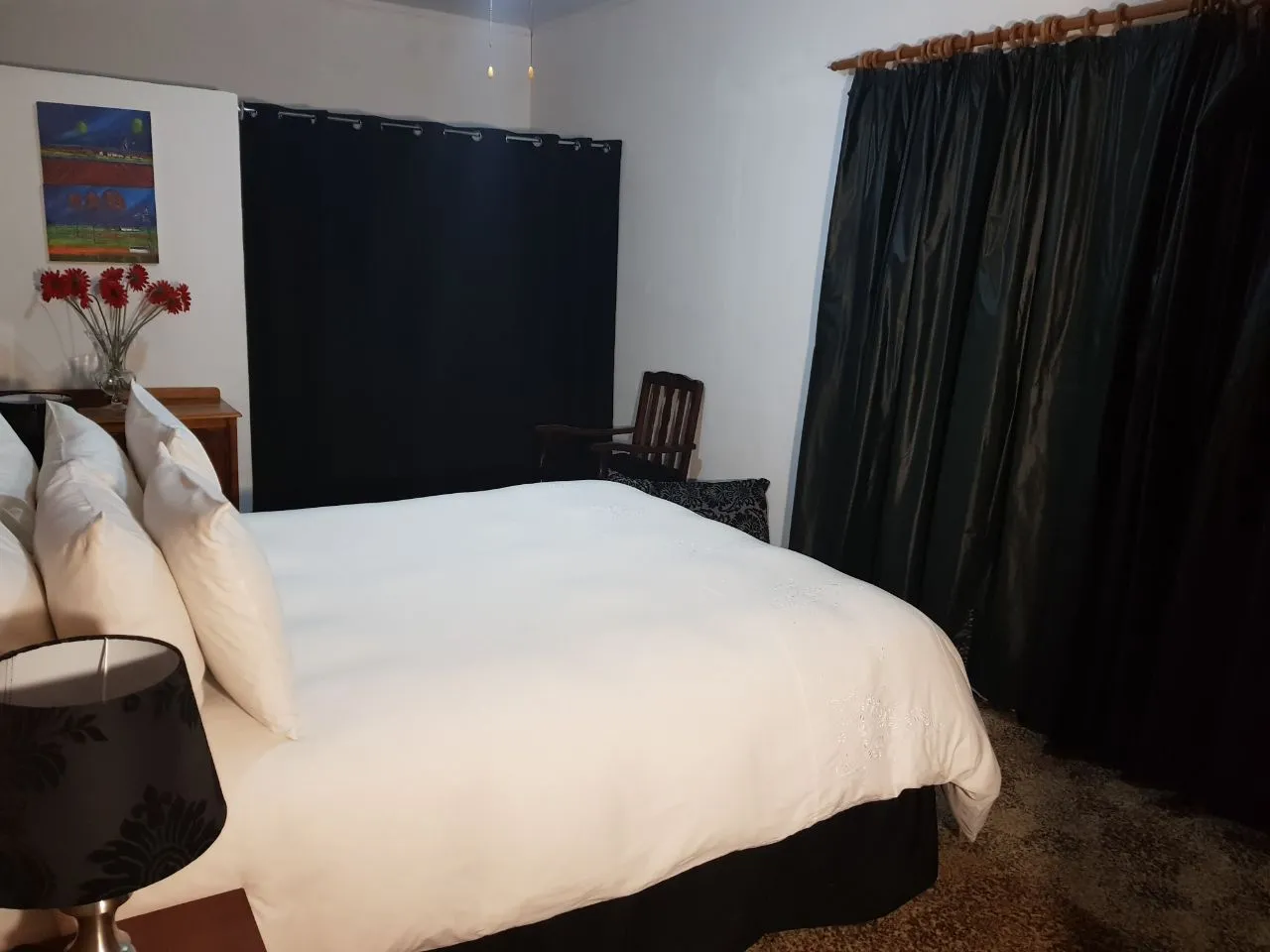Bedroom with white bed black curtains and a painting of flowers