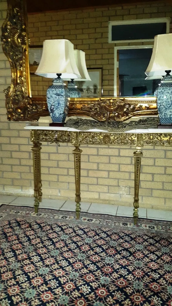 Ornate gold mirror with blue vases and lamps on a console table