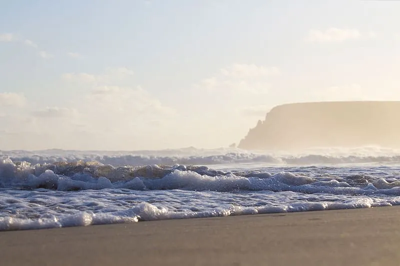 Waves crashing on a beach with a cliff in the background at sunset