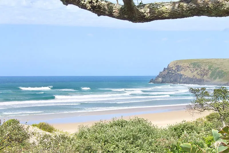 Beach with waves sandy shore greenery and cliff under a blue sky