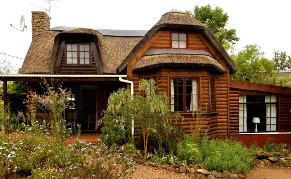 Wooden cottage with a thatched roof surrounded by flowers and greenery