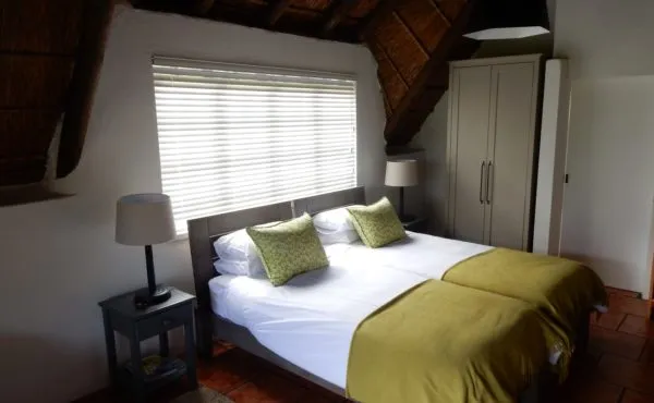 Cozy bedroom with two single beds green bedding and a thatched ceiling