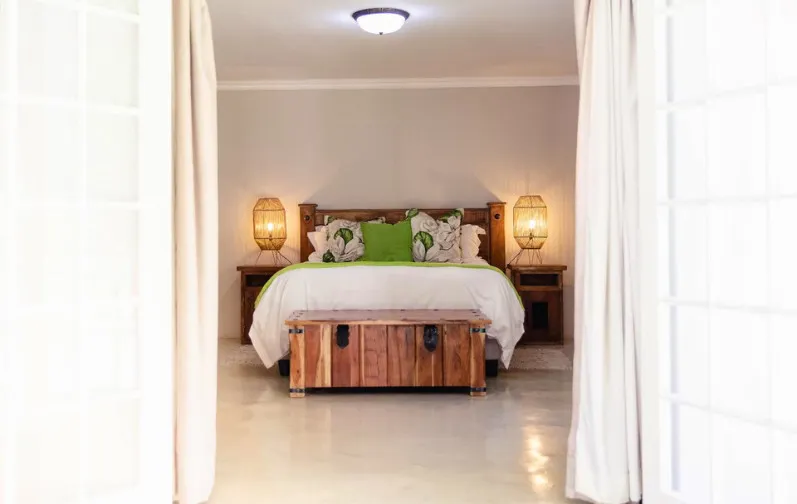 Bedroom with a large bed green pillows and wooden furniture viewed through a doorway