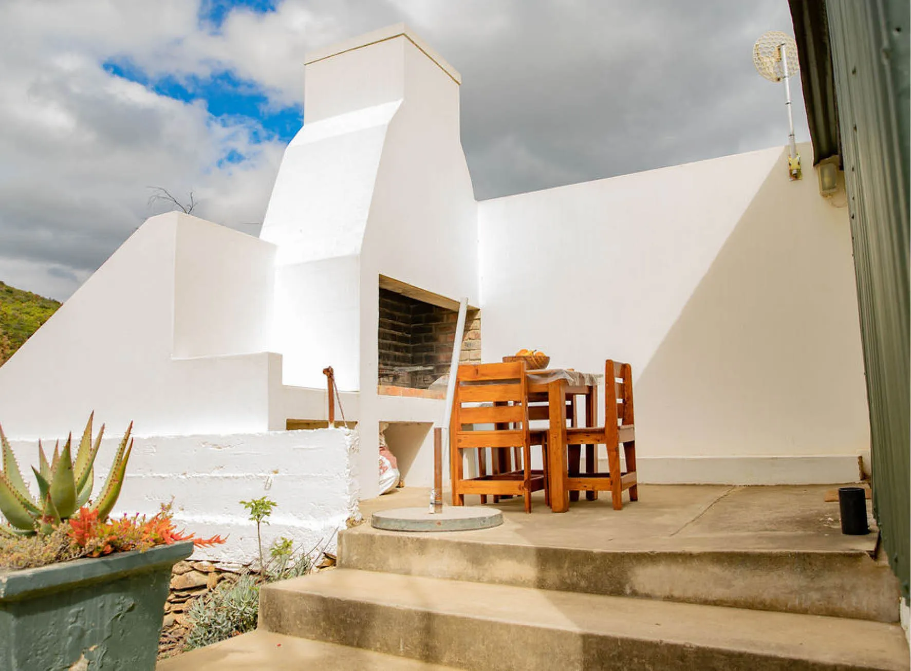 Outdoor patio with white barbecue wooden table and chairs under cloudy sky