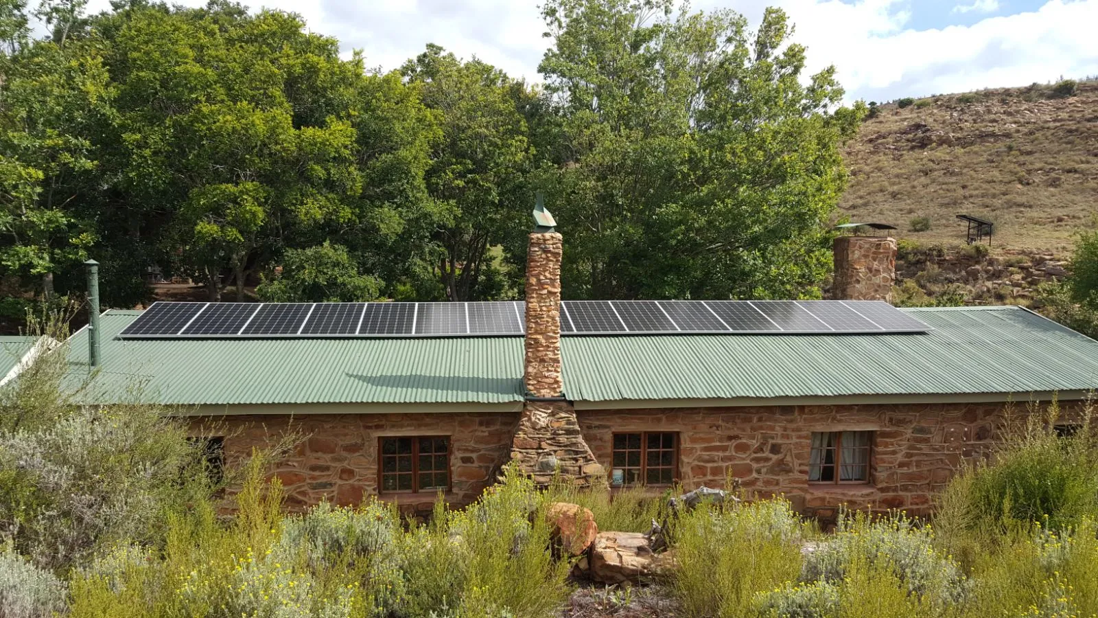 Stone house with solar panels on roof surrounded by greenery and trees