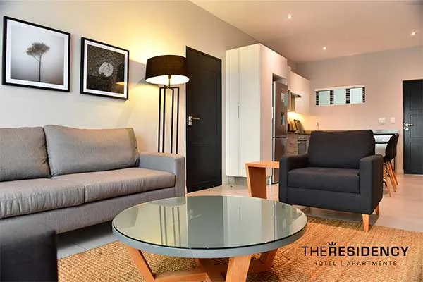 Modern living room with grey sofas glass table and kitchenette in background