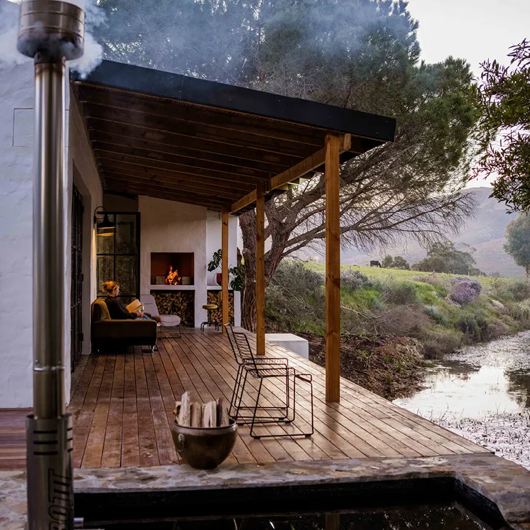 Wooden deck with furniture and a fireplace overlooking a river and trees