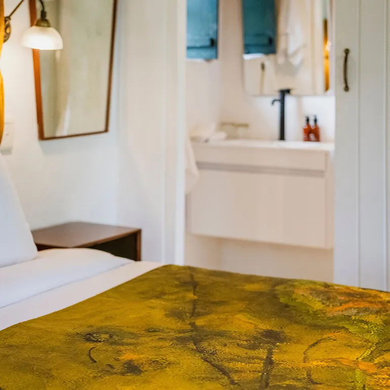 Bedroom with a bed nightstand and bathroom with sink and mirror in background