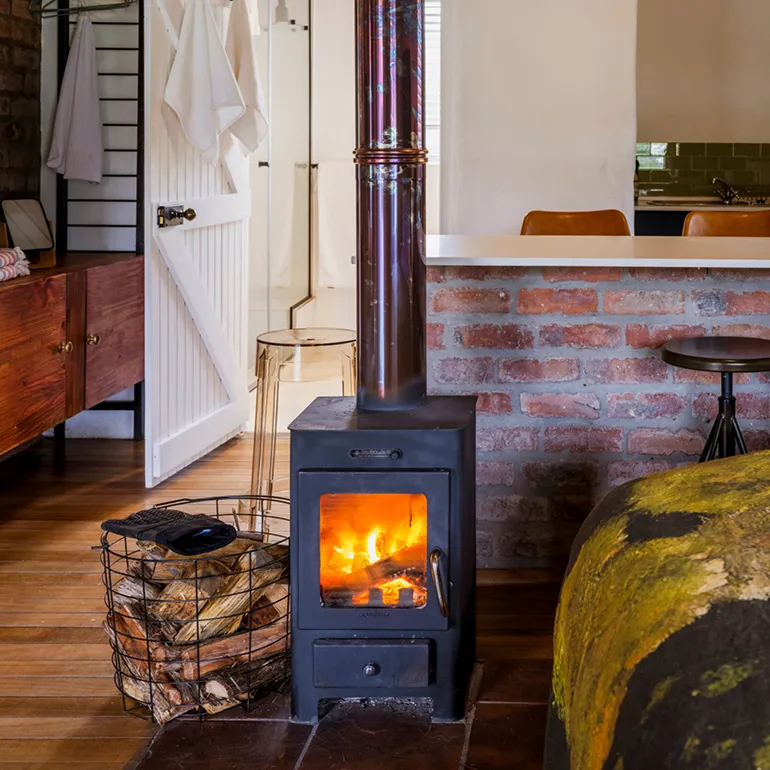 Wooden stove with fire in a cozy room with brick wall and furniture