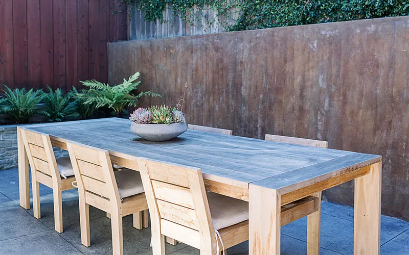 Wooden table and chairs on a patio with plants and a wooden fence