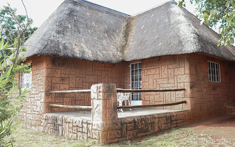 Thatchedroof house with stone walls and a small porch with a chair