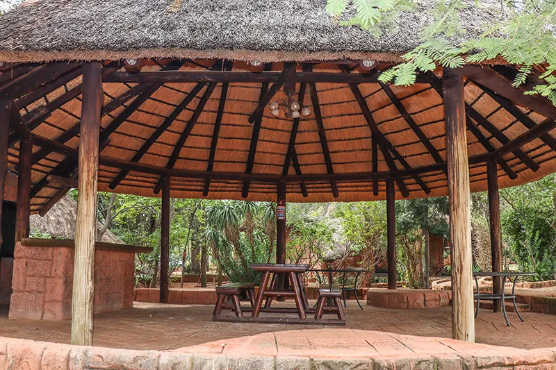 Wooden picnic area with a thatched roof in a lush garden setting
