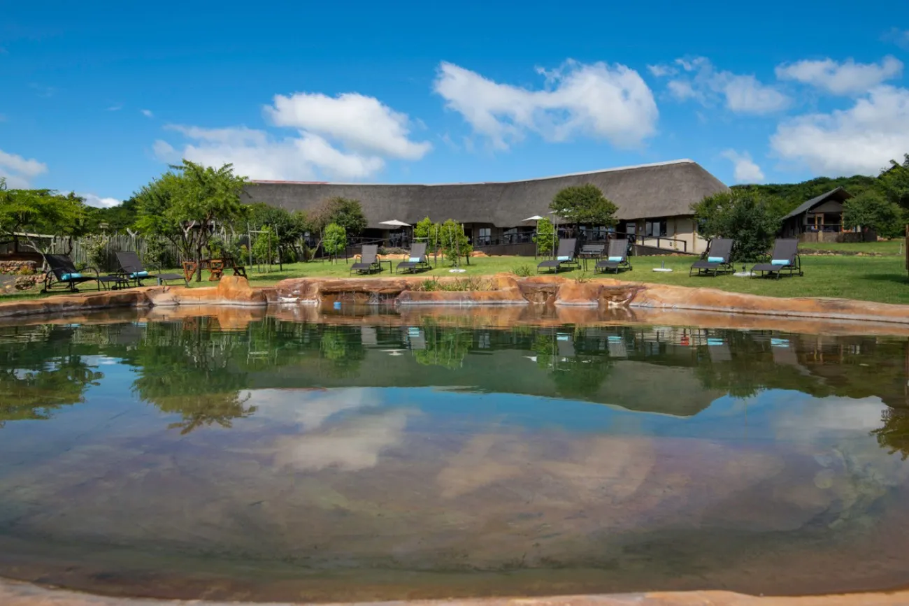 A pool with lounge chairs in front of a traditional African lodge