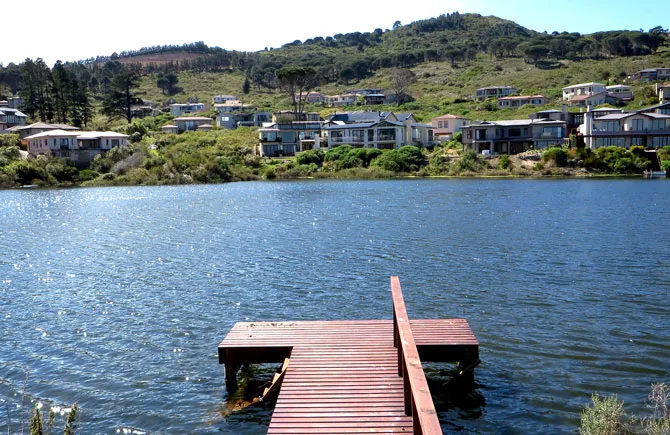 Wooden dock extending over a lake with houses and hills in the background