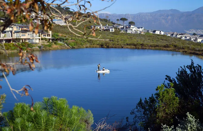 Person in a small boat on a lake with houses and mountains in background