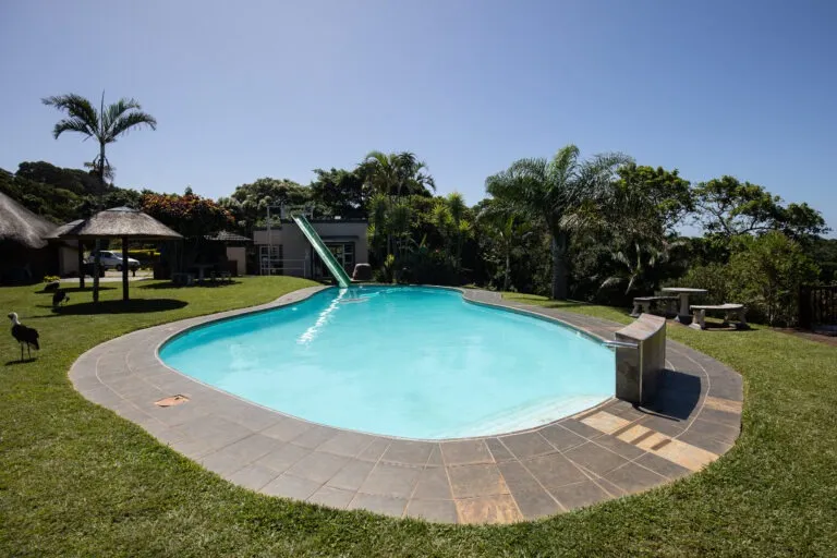 Swimming pool with slide in a garden setting with trees and benches