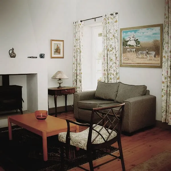 Cozy living room with armchair sofa and fireplace featuring floral curtains and artwork