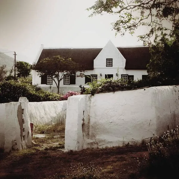 Whitewashed house with thatched roof and garden framed by trees