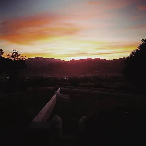 Sunset over mountains with trees and a fence in the foreground