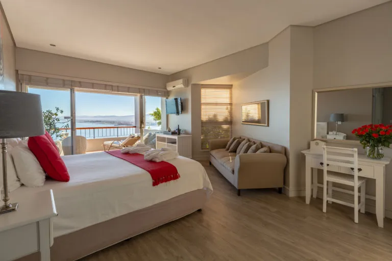 Modern bedroom with large window bed sofa desk and ocean view
