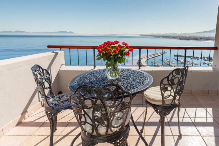 Wrought iron table with red flowers overlooking ocean and marina