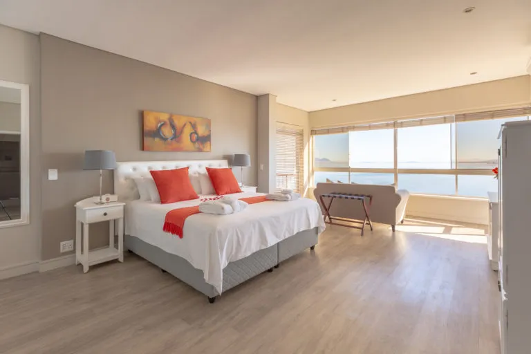 Modern bedroom with large windows white bed orange pillows and wooden floor