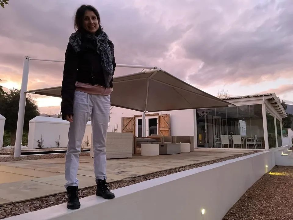 Woman standing on a low wall in front of a modern house at sunset